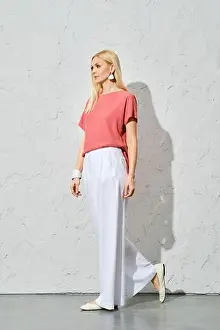 Blond Hair Prints: Trendy woman with blond hair in pink shirt and loose white trousers walking along white wall