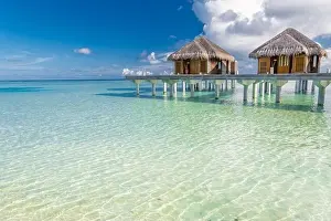 Tropical beach in Maldives with luxury over water bungalows or villas. Amazing sea lagoon with blue sky and clouds. Exotic travel destination