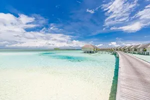 Tropical paradise: view of over water bungalows at a resort in the Maldives, Indian Ocean. Long jetty leading into water villas under blue tropic sky