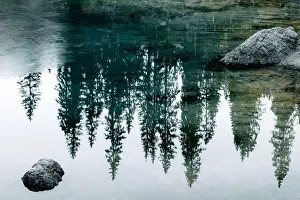 Turquoise frozen water of Lake Carezza (Karersee) in Western Dolomites, Italy. Beautiful close up view with stones and pines reflection