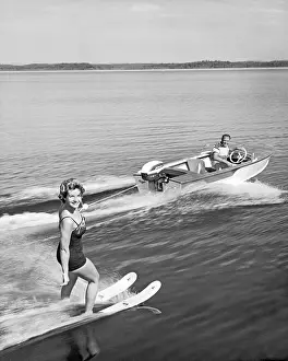 Wake Prints: United States: c. 1958 A pretty woman smiles at the camera as she holds on with one hand while water skiing on a lake