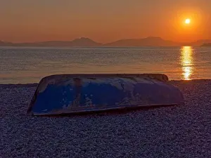 Blue Hour Prints: Upside Down. An old boat on the beach under the morning sun rising in early morning orange skies over the Corinthean
