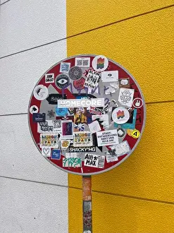 Stickers Prints: Urban stop sign covered in colorful stickers against a vibrant yellow and white background