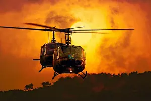 A utility military helicopter flying above the forest at sunset time