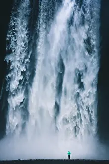 Instagram Prints: Vertical panorama view of hiker in colorful rain jacket standing in front of gigantic Skogafoss waterfall