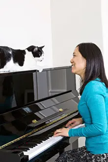 Perform Prints: Vertical photo of mature woman with her family cat on top of piano looking at each other while sitting at the piano