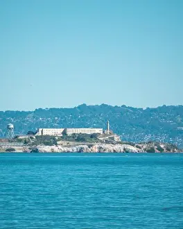 Prison Prints: A vertical shot of Alcatraz island with the sea view and forested mountain and sky background