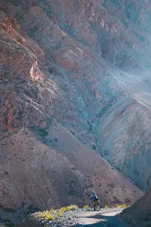 Grass Hill Prints: A vertical shot of a person with a bicycle surrounded by rocky mountains in a rural area