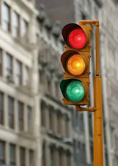 Illuminate Prints: Vertical traffic light with red yellow and green signals illuminated in an urban city background