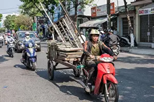 Indochina Prints: Vietnamese motorbike driver pulls wagon overloaded with building materials