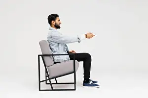 Obese Prints: Side view of Asian man sitting in the armchair while watching TV in the studio