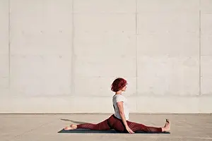 Gymnastic Prints: Side view of barefooted Woman with closed eyes in sportswear doing yoga in monkey pose on mat training alone on street