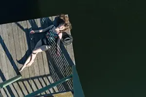 Faceless Prints: Top view of beautiful Woman in black swimsuit and hat lying down on wooden pier of lake on clear blue sky