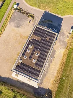 Top view of building with solar roof surrounded by an open area and fields