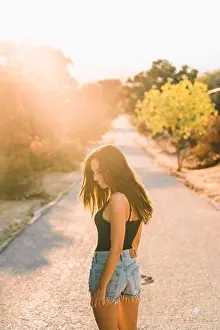 Blurred Background Prints: Back view of content beautiful Woman in jean shorts looking over shoulder while walking along scenic countryside road
