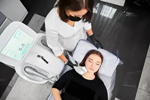 Rejuvenation Prints: Top view of cosmetologist in medical mask using Ultraformer device while performing face lifting procedure