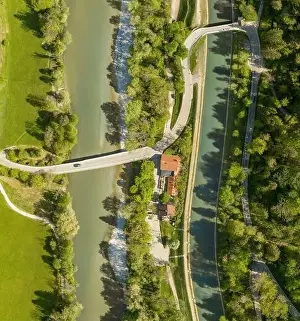 Top view from a drone at a driving car at a bridge over a river with a neaby forest and a house