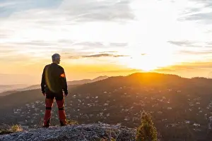 Unrecognizable Prints: Back view of elderly man in casual outfit sitting on rocky cliff and admiring view of majestic mountains