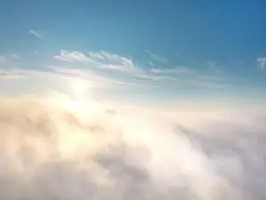 View from above of fog or clouds with clear blue sky and rising sun in the background