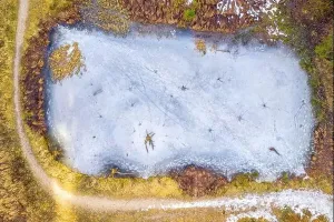Blue Ice Prints: Top view of frozen lake covered with blue ice and surrounded by a snowy path at a beautiful winter landscape
