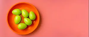Top view of green Easter eggs in a bright plate on vibrang orange and red background