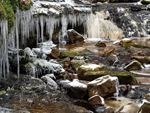 Flowing Water Prints: View of heavy icicles hanging from rocky banks above a frozen river