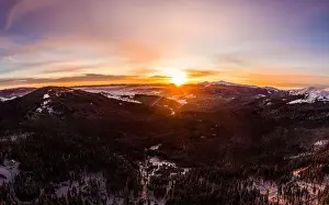 Hill Glacier Prints: Top view of a magical view of a mountain winter forest with thick fir trees and hills in a beautiful pink winter sunset