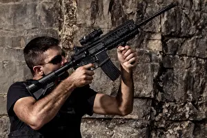 Mafia Prints: View of a menacing man pointing a machine gun in a black shirt and dark shades on a stone quarry