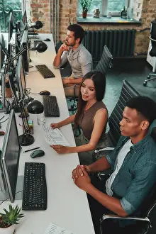 Coworker Prints: Top view of multiethnic team working on computers and talking with each other while sitting in modern open space