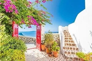 Images Dated 12th October 2019: View on Oia in Santorini, through red door or gate. Stone stairs with flowers under blue sky