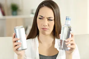 Choosing Prints: Front view portrait of a confused girl deciding between soda refreshment and water bottle at home