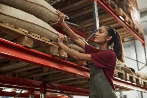 Burlap Prints: Side view portrait of smiling young woman working in warehouse at coffee roastery and checking burlap coffee bags