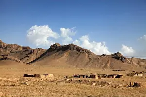 Desolate Prints: View of sun-baked mud houses nestled in a desolate landscape with the rugged mountains under a blue sky dotted with
