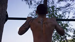 Back View Prints: Back view of tattooed man doing pull-ups while having workout in picturesque autumn park
