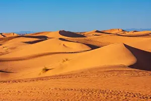 Ripples Prints: View of the vast orange sand dunes of Erg Chebbi under a clear blue sky with distant mountains on the horizon