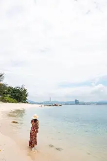 Unrecognizable Prints: Back view of Woman in hat and long dress walking in shallow water of tropical seaside on Wuzhizhou Island
