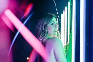 Contemplate Prints: Side view of young dreamy Woman reflecting between rows of glowing neon tubes while looking away