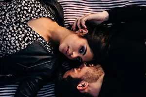 Pleasant Prints: Top view of young ethnic woman with makeup in leather jacket lying near bearded male beloved on textile