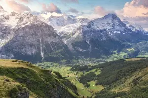 Surrounded Prints: Village with small houses on colorful green hillside with trees surrounded by high snowy ridge under blue sky with