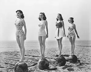 Poised Prints: Vintage black and white photography of 4 women in swimsuit standing tall on rocks at a beach