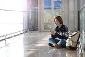 Dreams Prints: waiting for a flight at the airport. girl with a phone and a backpack sits on the floor