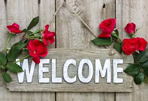 Weathered wood welcome sign hanging on wooden door with flower border of red roses