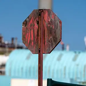 Faded Prints: Weathered wooden stop sign against industrial backdrop with clear blue sky Pincher Creek
