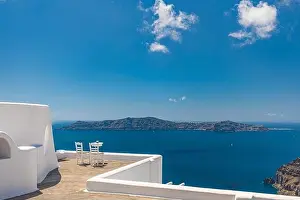 White architecture on Santorini island, Greece. Outdoor restaurant under a fantastic landscape, chairs for couple. Romantic view, summer vacation