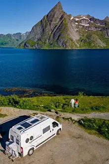 A white camper van parked near a couple enjoying the view of a stunning Norwegian fjord and mountain range