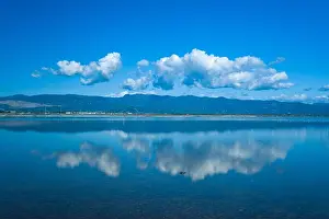 Stillness Prints: White cumulus clouds are perfectly reflected on the calm blue water of the Missolonghi salt marsh in western Greece