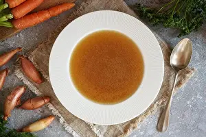 Paleo Prints: White plate or soup bowl with beef bone broth, with fresh vegetables in the background