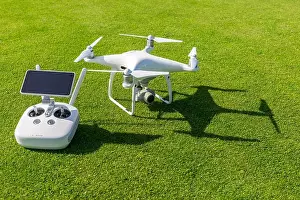 Remote Control Prints: White professional quadcopter drone camera with remote control from above against green grass in background