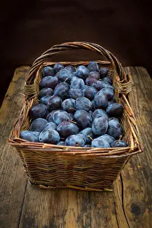 Interior View Prints: Wicker basket of organic plums, wooden table