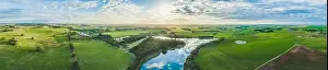 Wide aerial panorama of river flowing through grasslands, meadows, and pastures in Australia at sunset